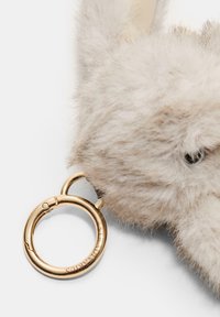 Porte-clés en peluche beige avec un design de lapin, quincaillerie en métal doré et un anneau de fixation circulaire. Des détails de surface texturée et douce sont visibles.