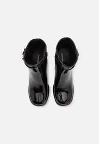 Botas de tobillo de charol negro con una superficie lisa y brillante, que cuentan con una cremallera lateral y una punta redondeada. El forro interior es suave y negro.
