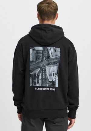 Sort hættejakke med et stort, gråt luftfoto tryk på ryggen. Designet viser bybygninger og et gadeskema, med teksten "BLEND SINCE 1993".