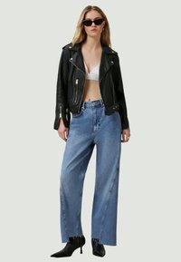 Jaqueta de motociclista de couro preta, top cropped branco, jeans largos azul claro e sapatilhas pretas de bico fino. Óculos de sol completam o visual.