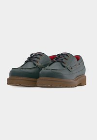 Σκούρα πράσινα δερμάτινα παπούτσια χαμηλού ύψους με χοντρές καφέ σόλες και μαύρα κορδόνια, με κόκκινη εσωτερική επένδυση και διακοσμητικές ραφές.