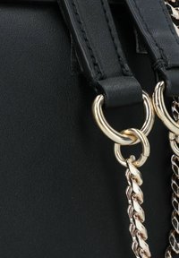 Borsa a mano in pelle nera con due manici piatti e hardware dorato, con un accento in catena attaccato attraverso anelli circolari.