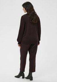 Bordeauxkleurige pullover met geribbelde mouwen, gecombineerd met bijpassende bordeauxkleurige broek en zwarte enkellaarsjes. Soepele textuur en een relaxte pasvorm.
