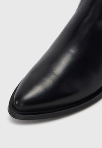 Μαύρο δερμάτινο μποτάκι αστραγάλου με μυτερή μύτη, λεία υφή και μινιμαλιστικό σχεδιασμό. Διαθέτει ανθεκτική ελαστική σόλα και διακριτικές ραφές.