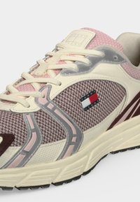 Κοντινό πλάνο ενός μπεζ και ροζ sneaker Tommy Jeans με διχτυωτό ύφασμα, κρεμ κορδόνια και λευκή και γκρι σόλα.