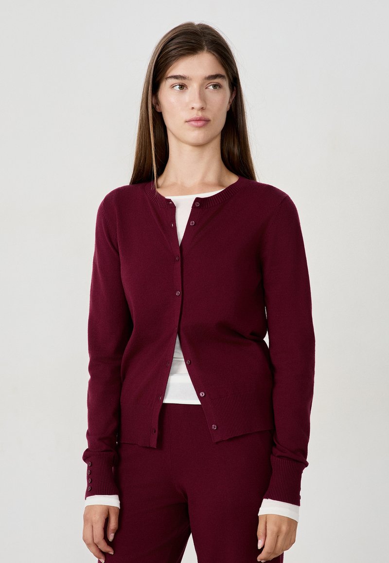 Cardigan bourgogne en tissu doux, avec un col rond, une fermeture à boutons sur le devant, des manches longues et des poignets et un ourlet côtelés.