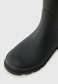 Black waterproof rubber boot with a smooth texture, rounded toe, and a thick, ridged black sole for traction.