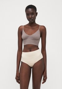Top court marron à côtes avec des bretelles fines et des sous-vêtements beiges taille haute. Texture lisse avec un design ajusté, sans motifs ni accents visibles.