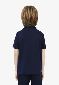 Granatowa koszulka polo z krótkim rękawem, klasycznym kołnierzykiem, gładką teksturą oraz małą metką na dolnym wykończeniu.