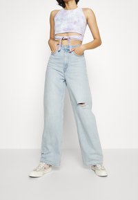 Violetti siteen värjätty crop-top, jossa on etumainen solmitys, yhdistettynä korkeavyötäröisiin vaaleansinisiin leveälahkeisiin farkkuihin, joissa on polvivaurio. Valkoiset tennarit viimeistelevät asun.