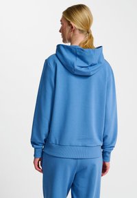 Ljusblå lustjacka av mjukt material, med snörning i huvan, ribbade ärmslut och nederkant. Enkelt design utan mönster.