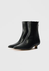 Bottines noires en cuir avec un bout pointu, un léger talon, une texture lisse et un design minimaliste.