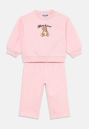 Rozā kokvilnas bērnu apģērbs, kas sastāv no kreklu ar apaļu kakla izgriezumu, uz kura attēlots tējas lācis, un atbilstošām legingām. Augšdaļai ir ribota apkakle un apakšmala.