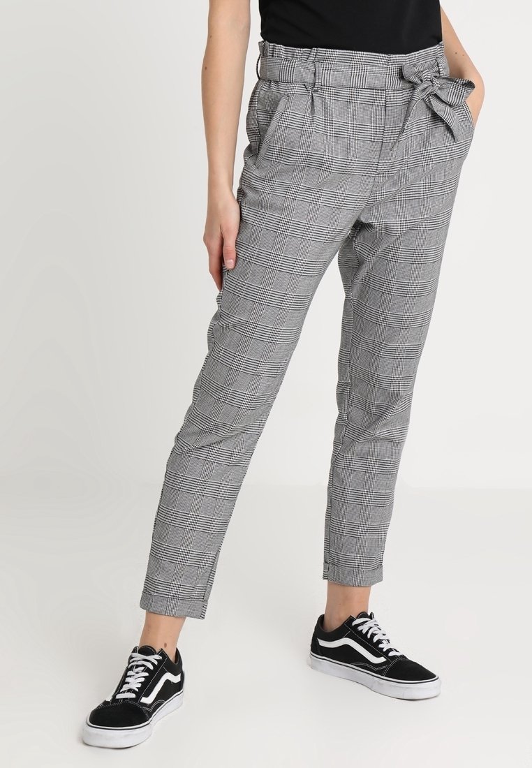 Pantalons à carreaux gris et noirs avec une taille haute, une ceinture à nouer et des poches latérales, associés à des baskets noires avec des accents blancs.
