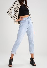 Cardigan de lunares en crema y negro, top corto negro, jeans de tiro alto azul claro remangados en los puños y botas de tacón negro hasta el tobillo.