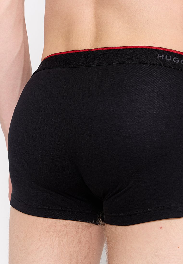 Mężczyzna w czarnych bokserkach Hugo Boss z czerwoną elastyczną talią, pokazany z tyłu, podkreślający dopasowanie i fakturę materiału.