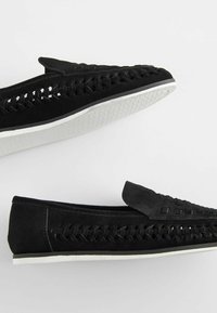 Black suede loafers featuring woven details along the sides, a rounded toe, and a white rubber sole with a textured pattern.