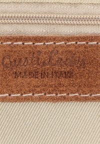 Patch en cuir suédé marron avec bords cousus sur tissu beige, estampillé des textes "Quiti Leather" et "Made in Italy".