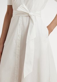 Biele košeľové šaty z bavlny, s gombíkmi na prednej strane, krátkymi rukávmi a opaskom viazaným v páse s hladkou textúrou.