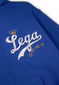 Felpa blu con ricami bianchi e dorati. Il design include testo stilizzato "Lega" e "GRMY" con un'icona di corona sopra. Texture morbida.