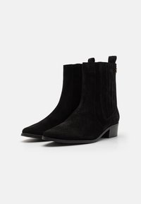 Czarne zamszowe botki za kostkę z wydłużonym noskiem, żebrowanymi bocznymi panelami i niskim, blokowym obcasem. Posiadają pętelkę umożliwiającą łatwe zakładanie.