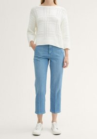 Vit stickad tröja med texturmönster och ribbat avslut, kombinerad med ljusblå ankellånga jeans och vita sneakers.