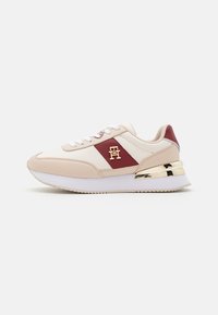 Jasnoróżowe sneakersy z białymi akcentami, złotymi elementami i bordowym paskiem. Posiadają teksturowaną podeszwę i sznurowany fason.