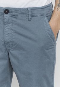 Világoskék chino nadrág tartós pamut keverékből, elöl gombos zárással, oldalsó zsebekkel és puha, texturált felülettel.