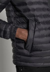 Svart puffjacka med kviltad design, elastiska manschetter och sidofickor. Slät, glänsande yta, lättviktig och isolerad för värme.