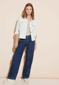 Helle Denimjacke mit Knöpfen, graues Oberteil, weit geschnittene dunkelblaue Jeans und beigefarbene Sneakers. Glatte Textur, lässiges Design, klare Linien.