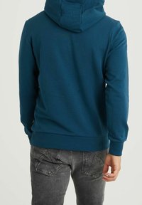 Felpa blu da uomo, tessuto texturizzato, cappuccio completo, orlo e polsini a coste, design semplice, abbinata a jeans grigio scuro con dettagli sulle tasche.