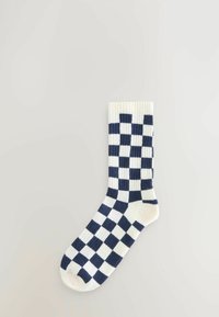 Calzino bianco con motivo a scacchiera blu navy, polsino a coste e superficie liscia. Presenta una punta arrotondata e una costruzione senza cuciture.