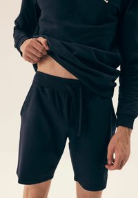 Granatowy sweatshirt i szorty wykonane z miękkiego materiału. Sweatshirt ma okrągły dekolt i długie rękawy; szorty mają elastyczny pasek w talii z sznurkiem.