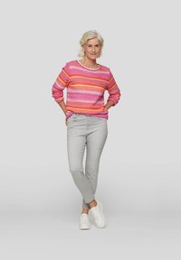 Mehrfarbiger gestreifter Pullover in Pink, Orange und Weiß mit langen Ärmeln, kombiniert mit hellgrauen Slim-Fit-Jeans und weißen Sneakern.