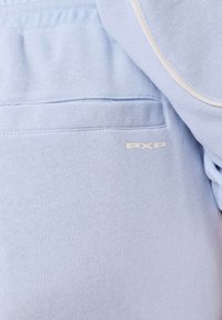 Lichtblauwe stof van dichtbij die een zak toont met ribbelrand en een klein "PXP" logo in crèmekleur.
