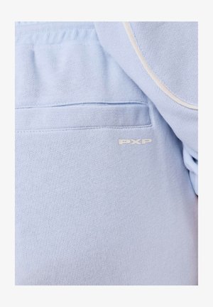 Nahaufnahme eines hellblauen Stoffes, der eine Tasche mit Rippbesatz und kleinem "PXP"-Logo in Cremefarbe zeigt.