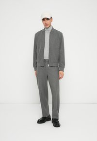 Giacca bomber grigia textured sopra un dolcevita grigio, abbinata a pantaloni tapered grigi e scarpe nere. Cappello beige chiaro.