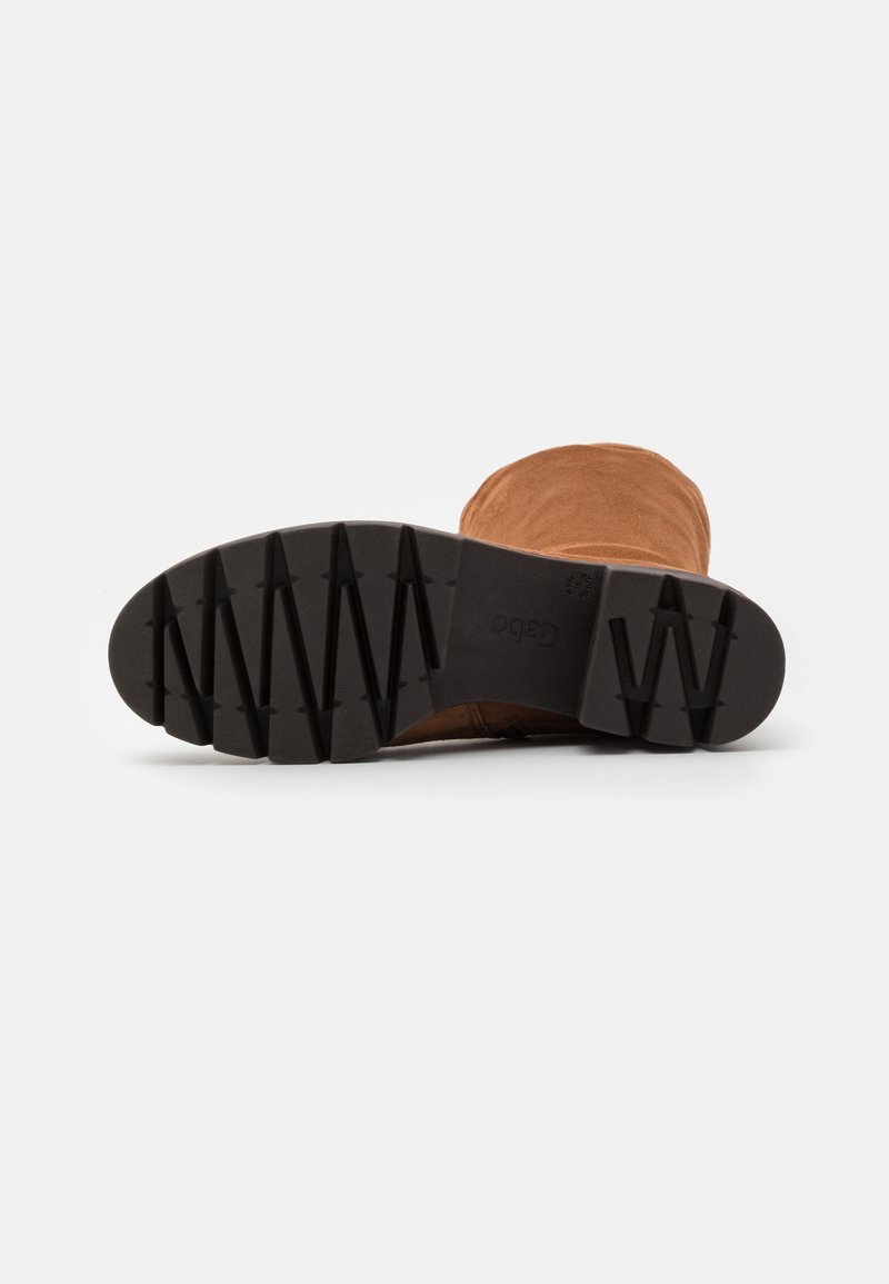 Bruine suède enkelboot met een gestructureerde zwarte rubberen zool met een zigzagpatroon voor grip. Naadloos ontwerp zonder zichtbare veters of sluitingen.