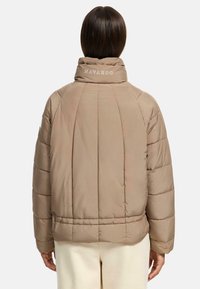 Beige pufferjack met een hoge kraag en geborduurd "NAVAHOO" logo. Beschikt over gequiltte secties en een iets cropped ontwerp.