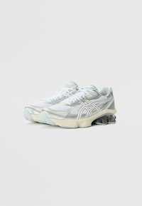 Light gray running shoes with synthetic mesh upper, metallic accents, rounded toe, and cushioned sole. Features white laces and logo detail.