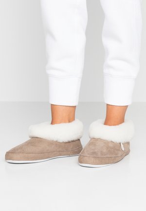 Mykebeige suedepumps med en luksuriøs hvit pelskant, rund tådesign og hvit gummisåle. Enkle sømdetaljer og sideskilt synlig.