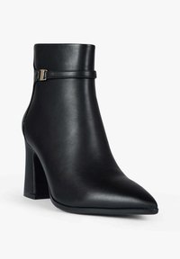 Stivaletto alla caviglia in pelle nera con punta appuntita, tacco robusto e dettaglio di fascia sottile con accessori metallici. Texture liscia, design minimalista.