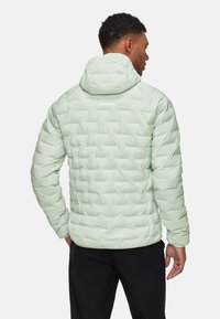 Hellgrüne isolierte Steppjacke mit Kapuze, mit gestepptem Muster und einem Logo auf der Rückseite, kombiniert mit einer schwarzen Hose.