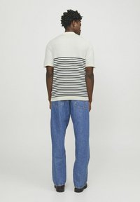 Herre kortærmet polo-shirt i lys creme med marineblå vandrette striber, parret med løse blå denimjeans og mørke sko.
