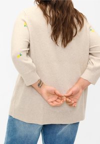 Maglione beige lavorato a maglia con maniche a tre quarti, caratterizzato da piccoli ricami di limoni verdi e gialli. Texture morbida e vestibilità rilassata.