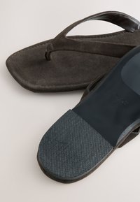 Brune ruskind flip-flop sandaler med flad sål og et tekstureret, gummibelagt fodseng for greb. Remmene har et minimalistisk design.