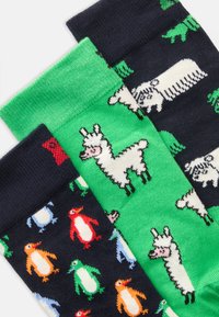 Three pairs of socks: green with llamas, navy with sheep, and black with colorful penguins. Knit texture, vibrant colors, playful patterns.