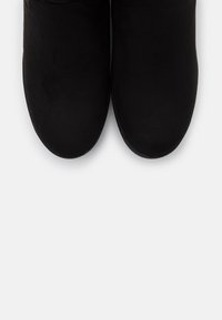 Une paire de bottines en suède noir avec des bouts ronds sur un fond blanc, présentée vue de dessus.