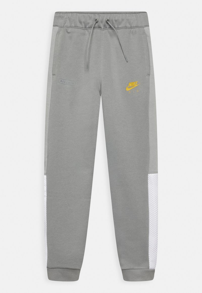 Šedé tepláky s páskem na stahování, žlutými logy Nike, bočními síťovanými panely a žebrovanými manžetami. Měkký materiál s volným střihem.