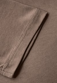 Brauner Baumwollstoff mit glatter Textur. Verfügt über eine umgebügelte Kante mit einem geraden Stich entlang der Naht.
